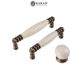 May include: Set of three ceramic cabinet knobs in a cream color with antique brass hardware. The knobs feature a rounded, oval shape and a decorative, spiral design.