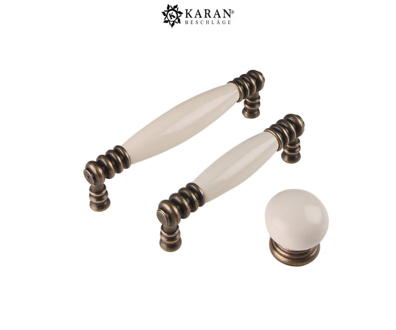 May include: Set of three ceramic cabinet knobs in a cream color with antique brass hardware. The knobs feature a rounded, oval shape and a decorative, spiral design.