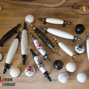 Può includere: Assortimento di pomelli e maniglie per cassetti in ceramica in vari stili e colori. I pomelli e le maniglie presentano disegni floreali, geometrici e astratti. Il testo "Hand Made" e "From Germany" è visibile nell'immagine.