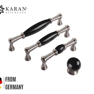 Könnte beinhalten: Drei schwarze Keramik-Schrankknöpfe mit silbernen Metallsockeln. Die Knöpfe sind in verschiedenen Größen und Formen. Der größte Knopf ist lang und oval. Der mittlere Knopf ist kürzer und oval. Der kleinste Knopf ist rund. Die Knöpfe sind alle aus hochwertigem Material gefertigt und haben ein elegantes, modernes Design.