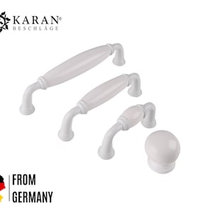 Könnte beinhalten: Satz von vier weißen Keramik-Schrankknöpfen und -griffen. Die Knöpfe und Griffe sind in verschiedenen Größen. Der größte Griff ist 30 cm lang. Der kleinste Knopf hat einen Durchmesser von 2,5 cm. KARAN BESCHLAGE ist oben im Bild gedruckt.