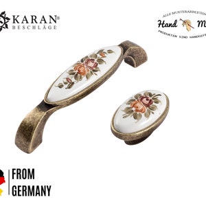 Könnte beinhalten: Zwei antike goldene Schrankknöpfe mit ovalen Porzellanplatten mit handbemalten Blumendesigns. Das Porzellan ist weiß mit orangefarbenen und braunen Blumen.