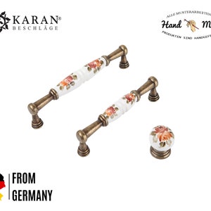 Peut inclure: Deux poignées de porte en laiton antique avec des poignées en céramique blanche ornées d'un motif floral. Les poignées sont rehaussées de fleurs orange et rouges. Un bouton assorti est également inclus.