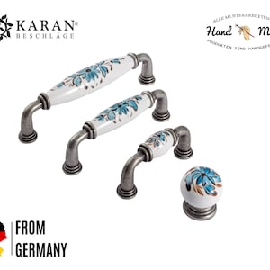 Pode incluir: Conjunto de quatro botões e puxadores de armário de cerâmica com base branca e design floral azul. A ferragem tem um acabamento prateado.  All Musterarbeiten an Hand Made Produkten sind handgefertigt.