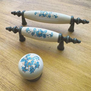 Può includere: Due pomelli per armadi in ceramica bianca con motivi floreali blu e dorati e ferramenta in bronzo antico. È mostrato anche un pomello rotondo abbinato.