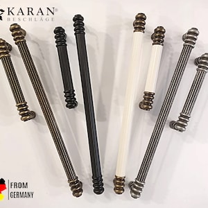 Może przedstawiać: Kolekcja dekoracyjnych klamek do drzwi w wykończeniach antycznego mosiądzu, matowej czerni i bieli. Klamki mają żebrowany design i pochodzą z Niemiec. Widoczna jest nazwa marki "KARAN BESCHLÄGE". Do drzwi.