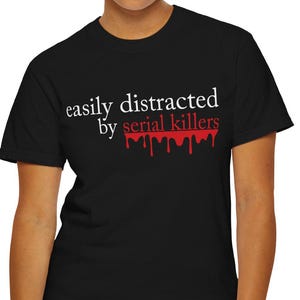 May include: Black t-shirt with the text "easily distracted by serial killers" in white and red. The words "serial killers" are in red with a dripping blood effect. The shirt is a crew neck and short-sleeved.