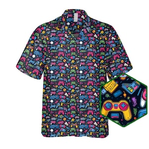 May include: A short-sleeved button-up shirt featuring a colourful pattern of video game controllers, buttons, and other gaming-related icons. The shirt is black with bright pink, blue, green, and yellow accents.