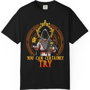 May include: Black t-shirt with a graphic of a hooded figure holding a book and a die in front of a circular design with the text "You Can Certainly Try".