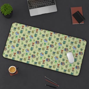 May include: A green desk mat with a repeating pattern of cartoon goblins wearing different colored hats. The goblins are holding a variety of objects, including a staff, a sword, and a book. The mat is surrounded by a black border.