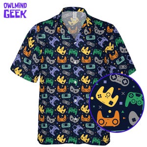 Op de afbeelding: Een shirt met korte mouwen met een marineblauwe achtergrond en een herhalend patroon van kleurrijke videogamecontrollers. Het shirt heeft een kraag en een close-up van het controllerpatroon. De tekst "OWL MIND GEEK" staat in de linkerbovenhoek.