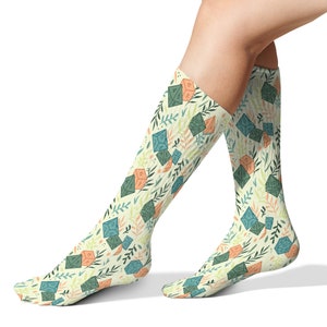 May include: A pair of knee-high socks with a white background and a pattern of green and orange dice with floral accents.