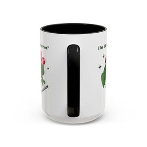 May include: White ceramic mug with a black interior and handle. The mug features a green cactus illustration with a pink flower and the text "I be like..." and "no worries".