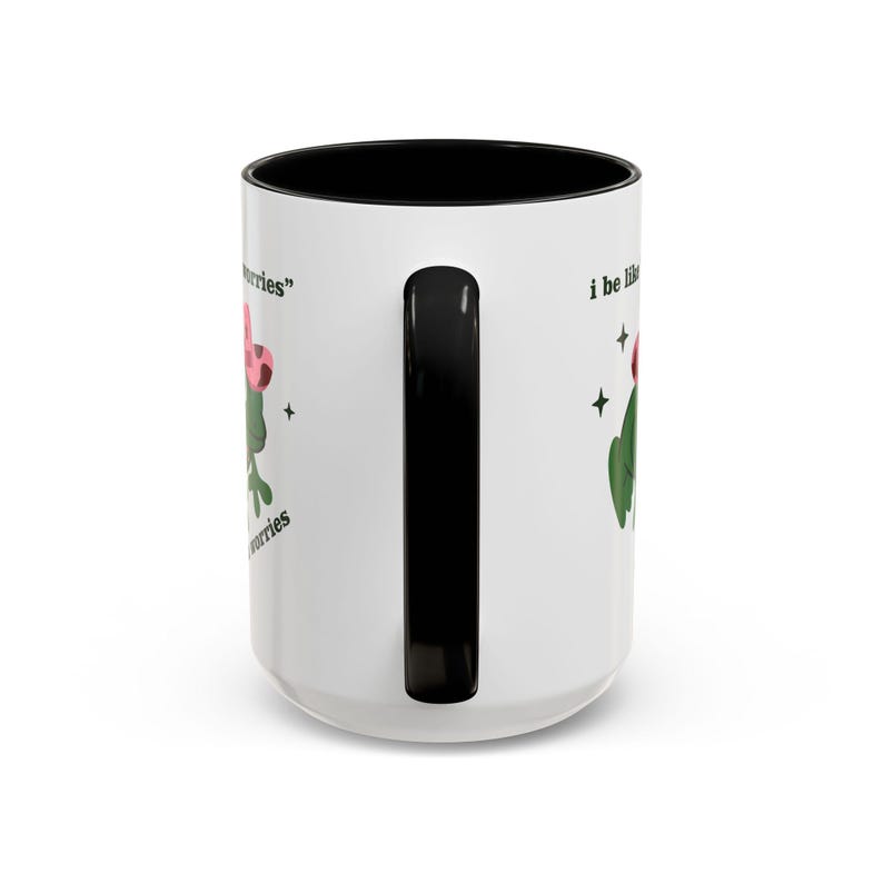May include: White ceramic mug with a black interior and handle. The mug features a green cactus illustration with a pink flower and the text "I be like..." and "no worries".