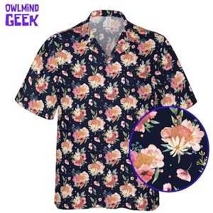 May include: Navy blue short-sleeved shirt with a floral pattern in pink, peach, and white. The shirt has a V-neck collar and a close-up of a floral design with a dice. The text "OWLMIN GEEK" is in the upper left corner.