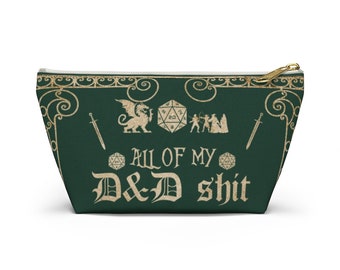 May include: A dark green pouch with a gold zip and the text "ALL OF MY D&D shit". The design includes illustrations of a dragon, dice, swords, and figures, ideal for storing gaming accessories.