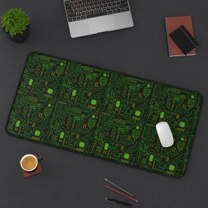 May include: A black and green mouse pad with a circuit board pattern. The mouse pad is on a black surface with a laptop, a notebook, a cup of coffee, and pencils.