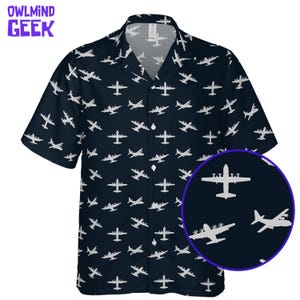 May include: A dark navy blue short-sleeve button-down shirt featuring an all-over repeating pattern of white airplanes in various flight orientations. The shirt has a classic collar and a front button placket. A circular inset shows a detail view.