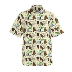 Pode incluir: Uma camisa de manga curta com bot&otilde;es em tom creme claro, apresentando uma estampa corrida de guaxinins castanhos, sanitas brancas, caixotes do lixo azuis e garrafas verdes. O texto TRASH PANDA est&aacute; impresso em verde por todo o padr&atilde;o.