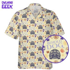 May include: A short-sleeve button-down shirt in a light cream color featuring an all-over print of tortoises and the text "BEHOLD DOG" in purple. The pattern includes small orange and purple floral accents and circular geometric symbols throughout.