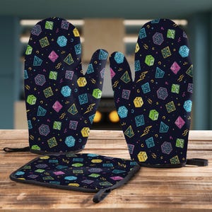 May include: A set of two oven mitts and a hot pad with a black background and a colorful dice pattern. The dice are outlined in neon colors and have different numbers on them.