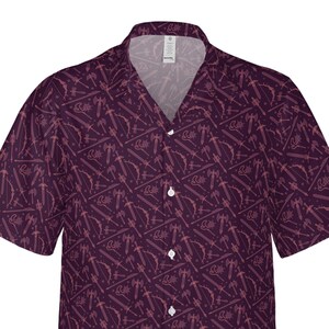 May include: A short-sleeved button-down shirt in a deep purple hue, patterned with light pink weapon illustrations. The design includes swords, axes, bows, and other fantasy-themed elements. The shirt has a classic collar and white buttons.