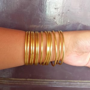 May include: A stack of gold-colored bangles on a person's wrist.