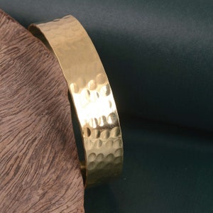 May include: A gold hammered metal cuff bracelet. The bracelet is thick and has a textured surface.