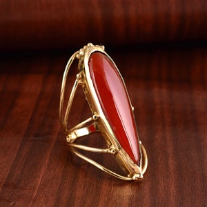 Op de afbeelding: Een gouden ring met een grote, traanvormige rode edelsteen die in een kooivormig ontwerp is gezet.