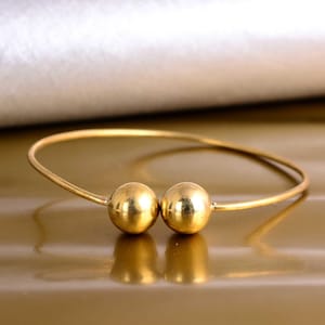 May include: A gold bangle bracelet with two large, round, gold beads.