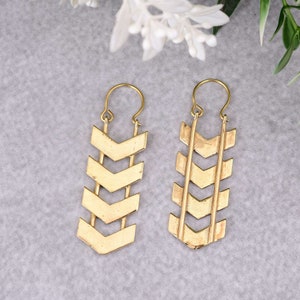 May include: A pair of gold-tone chevron dangle earrings. The earrings are made of metal and have a geometric design.