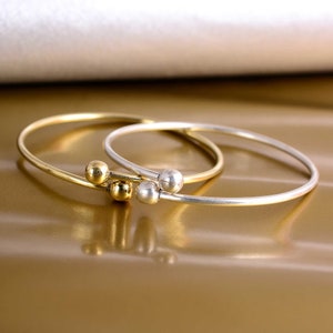 May include: Two simple bangle bracelets, one gold and one silver, with three small round beads at the connection point.