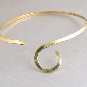 May include: A gold-toned metal choker necklace with a single, large, curved loop at the front.