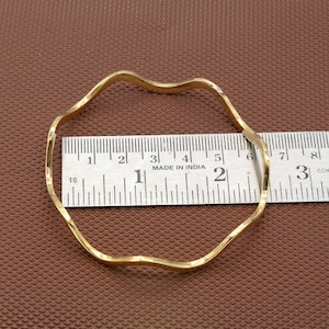 Puede incluir: Un brazalete ondulado de color dorado medido con una regla. La regla dice "MADE IN INDIA" y muestra que el brazalete tiene un diámetro de aproximadamente 5 cm.