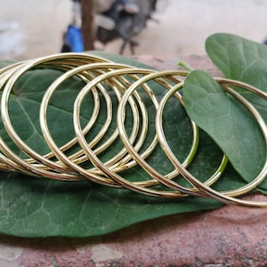 Può includere: Un set di dieci braccialetti rigidi dorati impilati uno sull'altro. I braccialetti sono disposti su una foglia verde.
