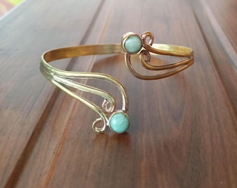 May include: A gold-tone cuff bracelet with two turquoise-coloured stones. The bracelet has a delicate, ornate design.