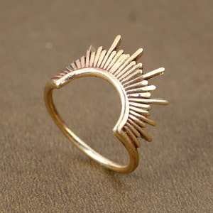 Peut inclure: Une bague en or avec un motif de soleil éclatant. La bague est ouverte à l'arrière et possède une bande lisse et arrondie.