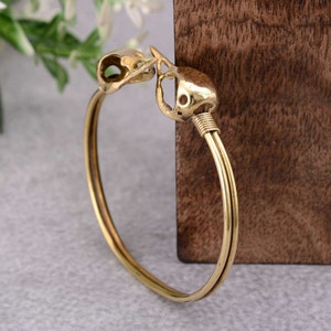 May include: A gold-toned bangle bracelet with two bird skull charms. The bracelet is made of two thin bands of metal.