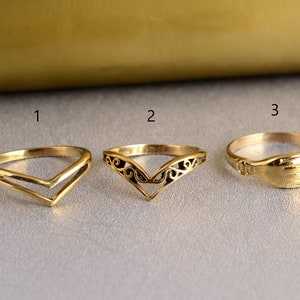May include: Three gold-toned rings with different designs. The first ring is a simple V-shape, the second ring is a more intricate V-shape with a floral design, and the third ring is a simple band with a raised hand design.