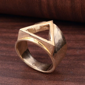May include: A gold ring with a geometric design. The ring has a triangular cutout in the centre, with a thick band. The ring has a polished finish and a vintage aesthetic.