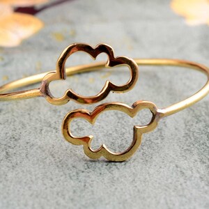 May include: A gold-toned metal bracelet with two cloud-shaped cutouts. The bracelet is open and adjustable.