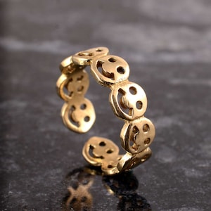 May include: Gold-toned adjustable ring with a repeating pattern of smiley faces.