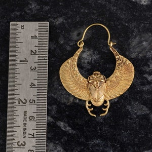 May include: Gold-colored earring with a scarab beetle design. The earring features a crescent-shaped wing design with intricate detailing. The earring measures approximately 3 inches in length.