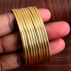 May include: A stack of 10 gold-colored metal bangles. The bangles are smooth and shiny.