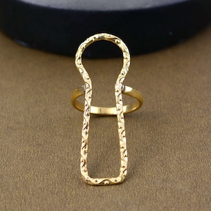 May include: Gold-toned ring with a unique open design. The ring is made of a thin metal band with a decorative pattern. The band is open at the top and bottom, creating a rectangular shape.
