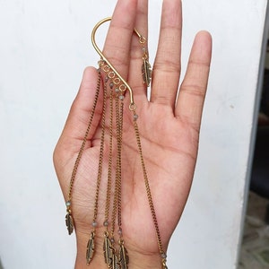 May include: Gold ear cuff with a long chain and multiple feather charms. The chain has small beads.