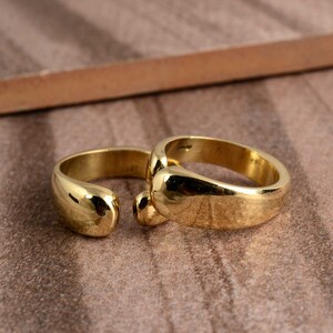 May include: Two gold-toned rings with a rounded, smooth design. The rings are stacked on top of each other.