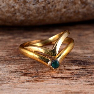 Op de afbeelding: Een gouden ring met een V-vormig ontwerp en een kleine groene edelsteen in het midden.