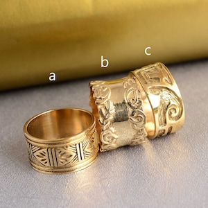 May include: Three gold-toned rings with intricate designs. The rings are stacked on top of each other, with the largest ring at the bottom and the smallest ring at the top.