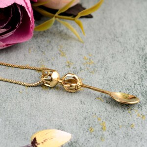 Può includere: Una collana dorata con un ciondolo a forma di cucchiaio con una parte superiore decorativa. Il ciondolo è un simbolo buddista tibetano tradizionale.